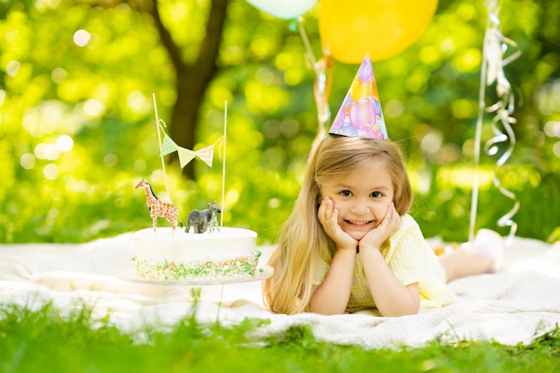 Piccola ragazza bionda sveglia che festeggia un compleanno in giardino una coperta sui palloncini colorati gras