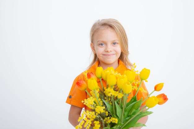 Piccola ragazza bionda sveglia in un vestito che tiene un mazzo dei fiori della molla su una priorità bassa bianca