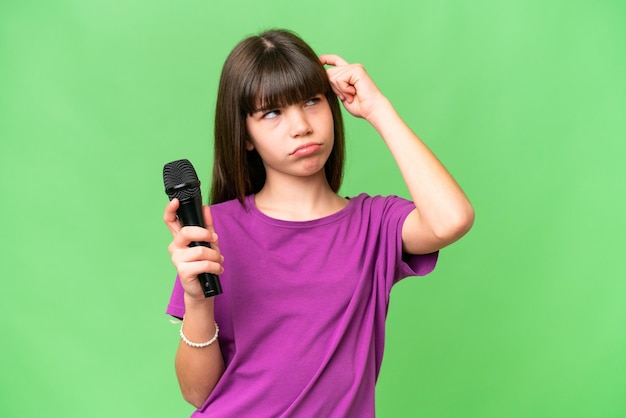 Piccola ragazza cantante che prende un microfono su sfondo isolato con dubbi e con espressione facciale confusa