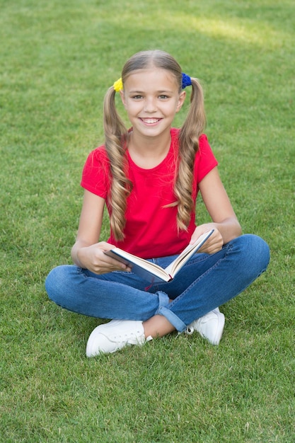 Piccola ragazza carina acconciatura libro di lettura rilassante natura sfondo torna al concetto di scuola