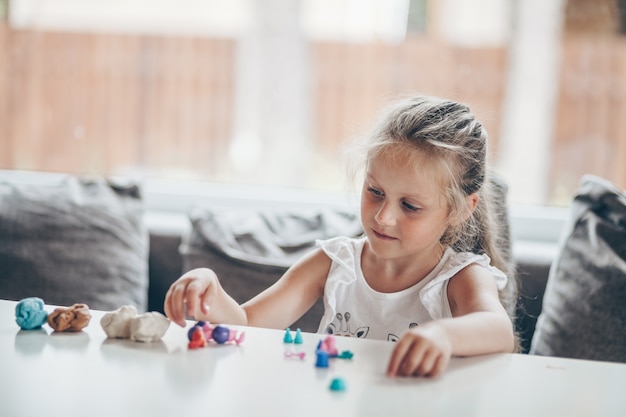 Piccola ragazza carina bambino in età prescolare che gioca giochi educativi con figure di plastilina che si preparano per la scuola