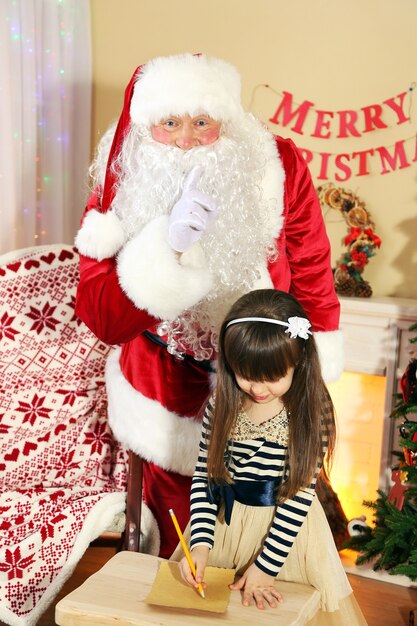 Piccola ragazza carina che scrive una lettera a Babbo Natale vicino all'albero di Natale a casa