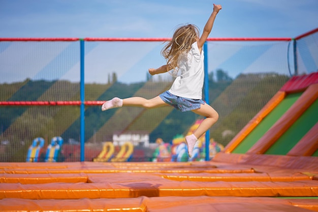 Piccola ragazza carina che si diverte all'aperto saltando sul trampolino nella zona dei bambini Ragazza felice che salta sul trampolino giallo nel parco dei divertimenti