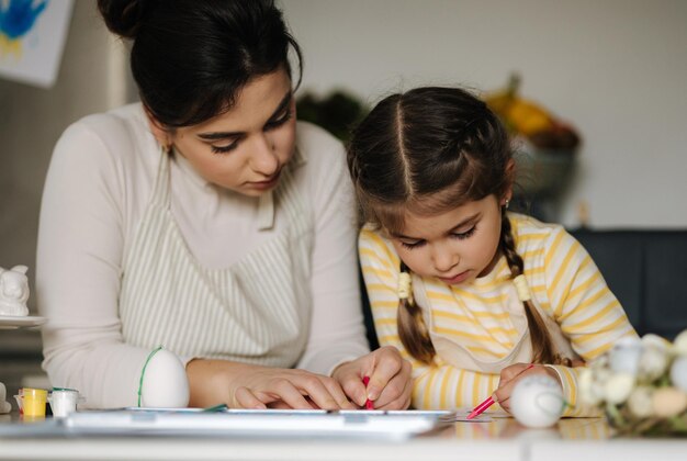 Piccola ragazza carina con sua madre che si prepara a dipingere le uova di Pasqua madre e figlia si guardano