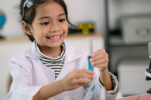 Piccola ragazza carina con un microscopio che tiene una bottiglia di laboratorio con un esperimento d'acqua studiano gli scienziati a scuola concetto di scienza dell'istruzione