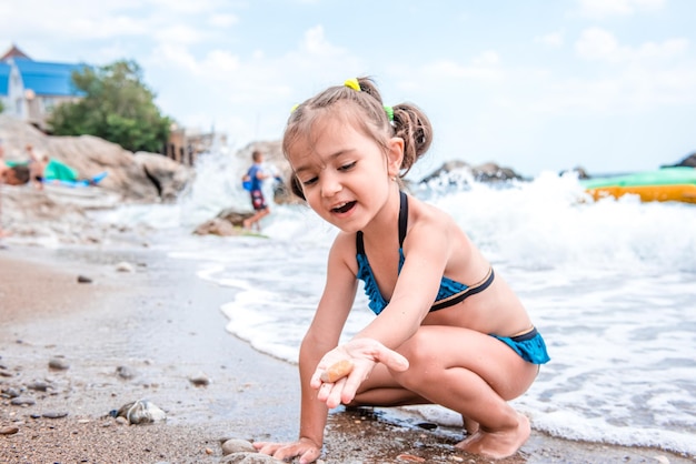 Piccola ragazza carina gioiosa in un costume da bagno blu in riva al mare Ritratto di una ragazza turismo per bambini