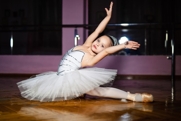Piccola ragazza carina in calzamaglia bianca che fa un nuovo movimento di balletto allo studio di danza