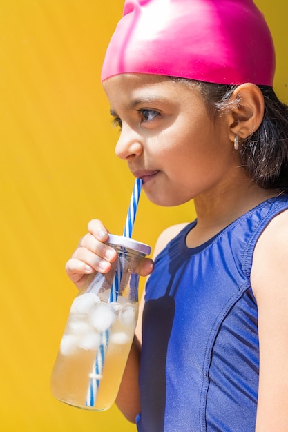 Piccola ragazza carina in costume da bagno che prende il sole mentre beve una limonata