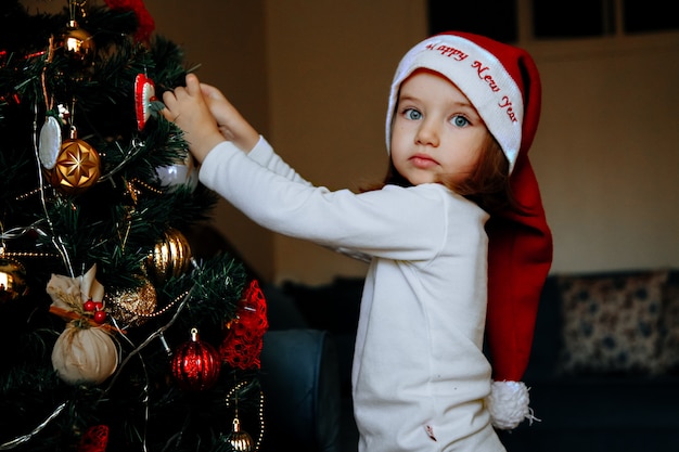 Piccola ragazza caucasica che decora un albero di Natale a casa.