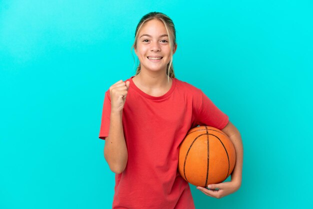Piccola ragazza caucasica che gioca a basket isolata su sfondo blu che celebra una vittoria in posizione di vincitore