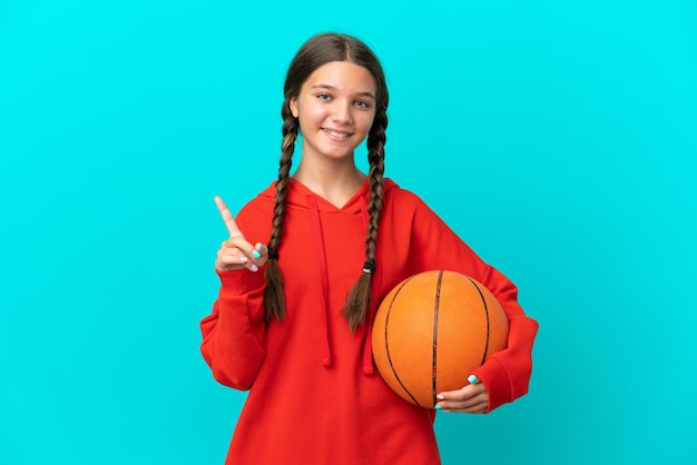 Piccola ragazza caucasica che gioca a basket isolata su sfondo blu che mostra e solleva un dito in segno del meglio