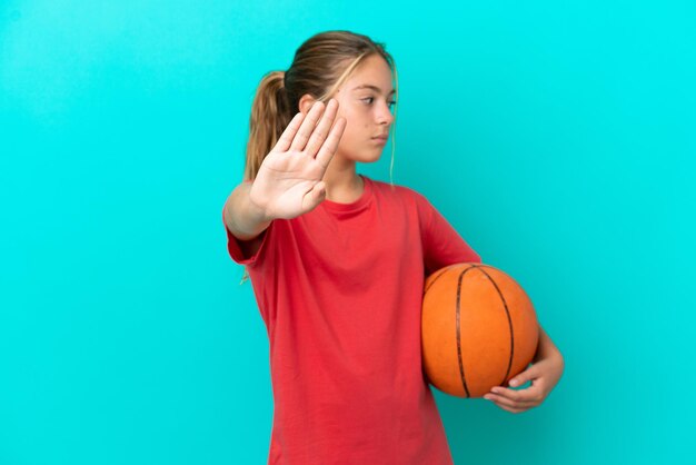 Piccola ragazza caucasica che gioca a basket isolata su sfondo blu facendo un gesto di arresto e delusa