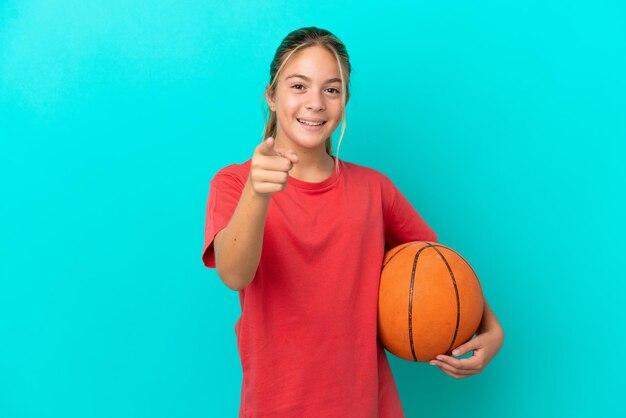 Piccola ragazza caucasica che gioca a basket isolata su sfondo blu sorpresa e puntata davanti