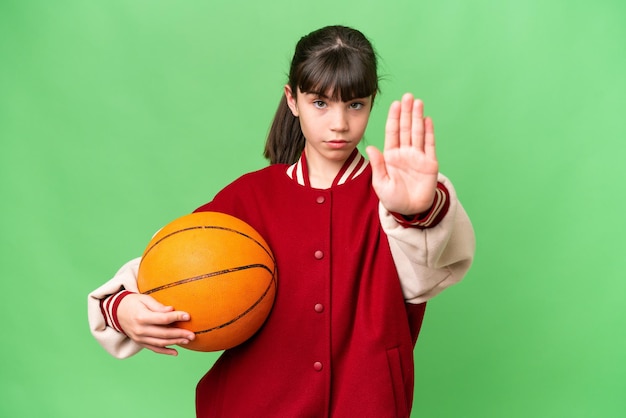 Piccola ragazza caucasica che gioca a basket su sfondo isolato facendo il gesto di arresto