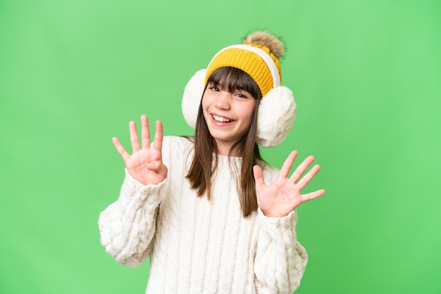Piccola ragazza caucasica che indossa manicotti invernali su sfondo isolato contando nove con le dita