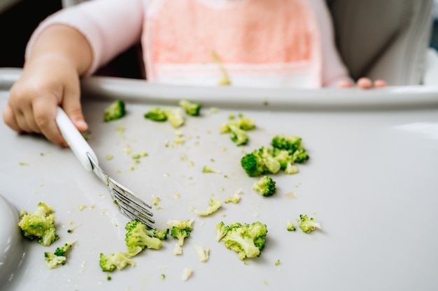 Piccola ragazza caucasica che raccoglie le verdure da un alimentatore in cucina con forchetta, vita sana per l'infanzia completamente vegana o vegetariana, concetto di svezzamento guidato dal bambino