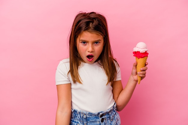 Piccola ragazza caucasica che tiene il gelato isolato sul rosa urlando molto arrabbiato e aggressivo.