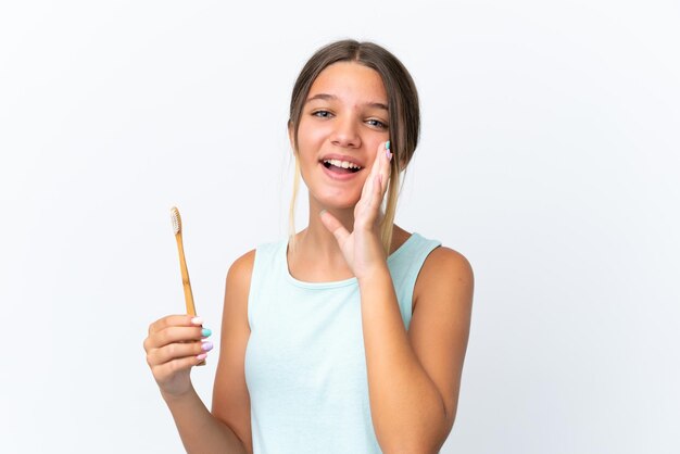 Piccola ragazza caucasica che tiene in mano uno spazzolino da denti isolato su sfondo bianco che grida con la bocca spalancata