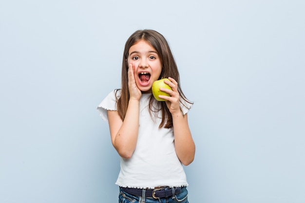 Piccola ragazza caucasica che tiene un gridare verde della mela eccitato alla parte anteriore.