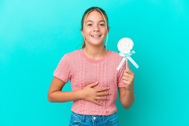 Piccola ragazza caucasica che tiene un lecca-lecca isolato su sfondo blu che sorride molto