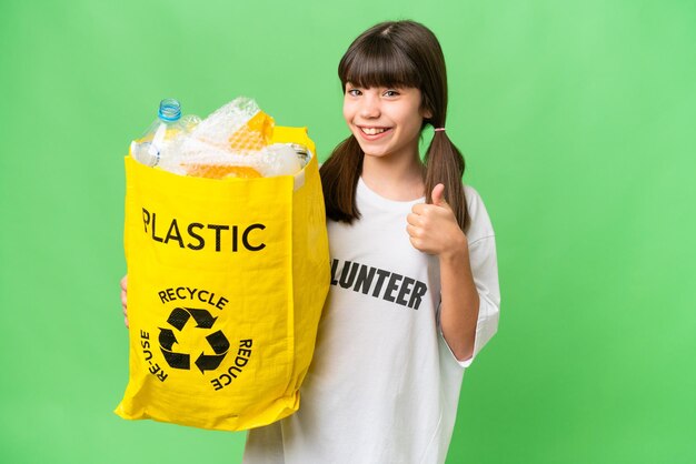 Piccola ragazza caucasica che tiene un sacchetto pieno di bottiglie di plastica da riciclare su sfondo isolato con il pollice in alto perché è successo qualcosa di buono