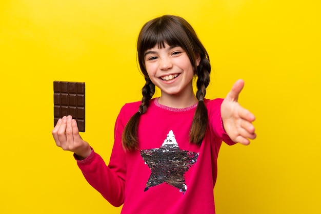 Piccola ragazza caucasica con cioccolato isolato su sfondo giallo che stringe la mano per chiudere un buon affare