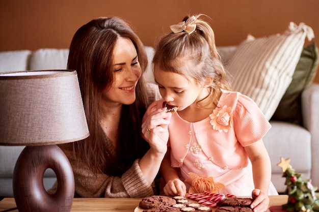 Piccola ragazza caucasica con madre che mangia gustosi biscotti di Natale Concetto di Natale in famiglia felice