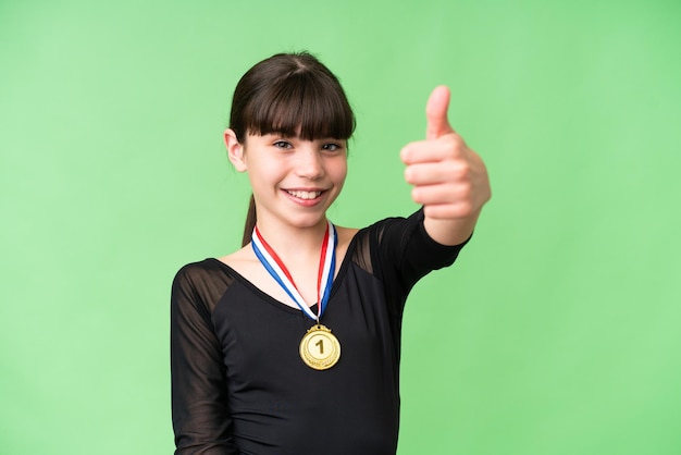 Piccola ragazza caucasica con medaglie su sfondo isolato dando un pollice in alto gesto