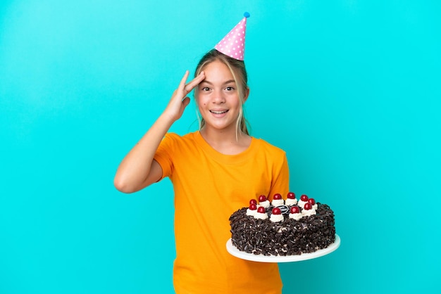 Piccola ragazza caucasica con torta di compleanno isolata su sfondo blu con espressione a sorpresa