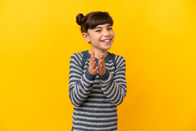 Piccola ragazza caucasica isolata su giallo che applaude dopo la presentazione in una conferenza