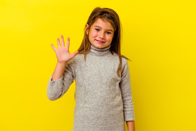 Piccola ragazza caucasica isolata su giallo sorridente allegro che mostra il numero cinque con le dita.