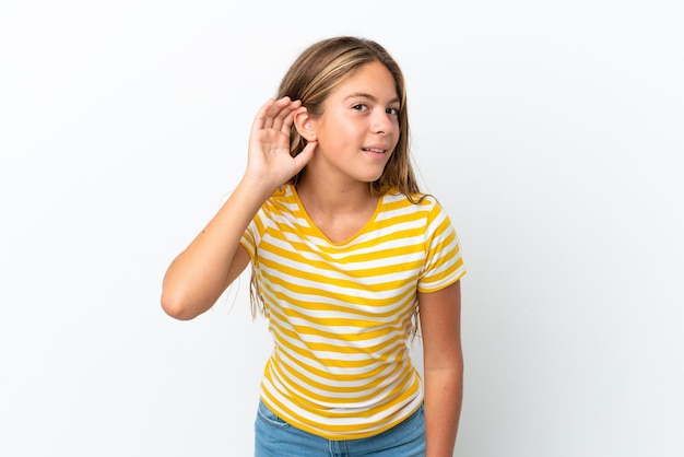 Piccola ragazza caucasica isolata su sfondo bianco che ascolta qualcosa mettendo la mano sull'orecchio