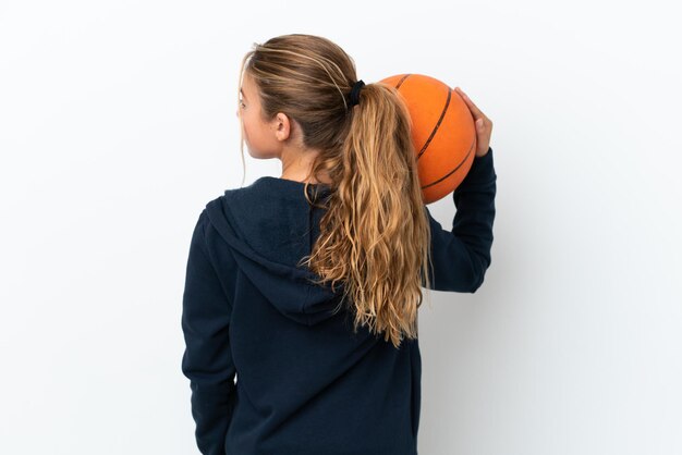 Piccola ragazza caucasica isolata su sfondo bianco che gioca a basket in posizione posteriore