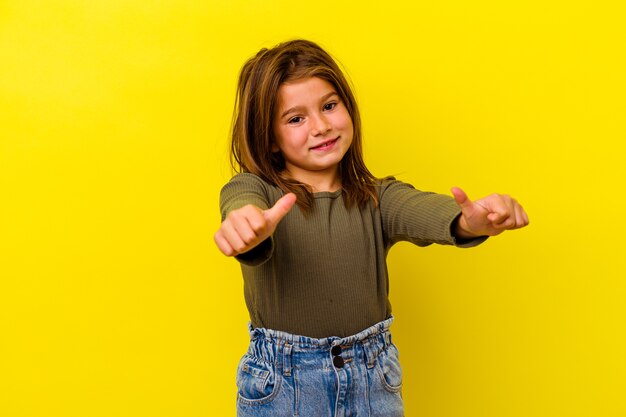 Piccola ragazza caucasica isolata su sfondo giallo alzando entrambi i pollici, sorridente e fiduciosa.