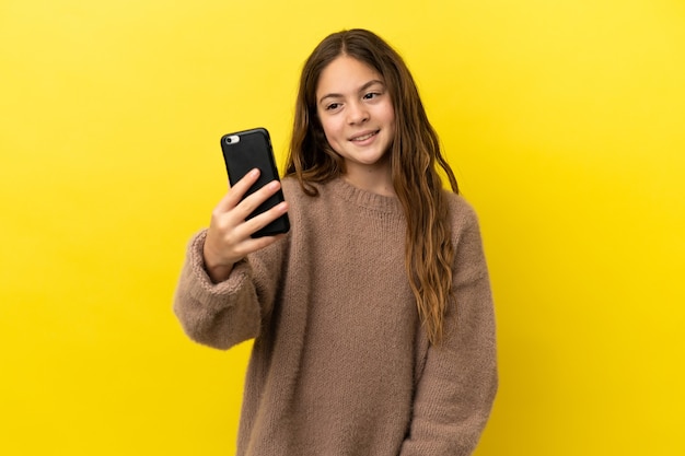 Piccola ragazza caucasica isolata su sfondo giallo che fa un selfie