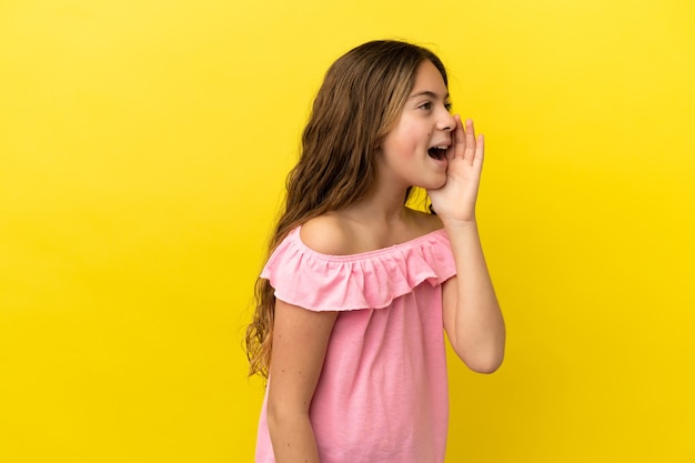 Piccola ragazza caucasica isolata su sfondo giallo che grida con la bocca spalancata di lato