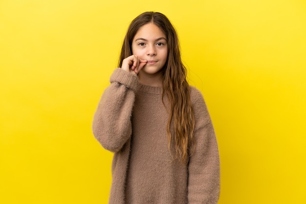 Piccola ragazza caucasica isolata su sfondo giallo che mostra un segno di gesto di silenzio