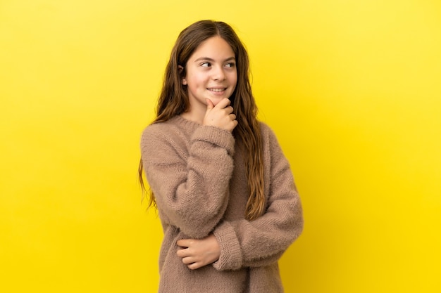 Piccola ragazza caucasica isolata su sfondo giallo che pensa a un'idea mentre guarda in alto