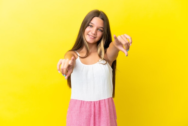 Piccola ragazza caucasica isolata su sfondo giallo che punta davanti con espressione felice