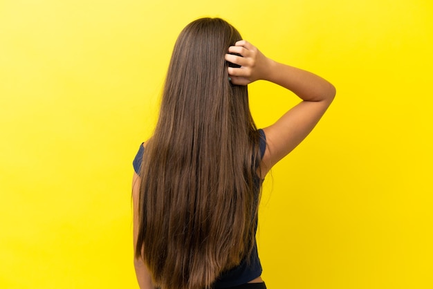 Piccola ragazza caucasica isolata su sfondo giallo nella posizione posteriore e nel pensiero