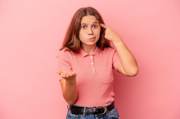 Piccola ragazza caucasica isolata su sfondo rosa che tiene e mostra un prodotto a portata di mano.