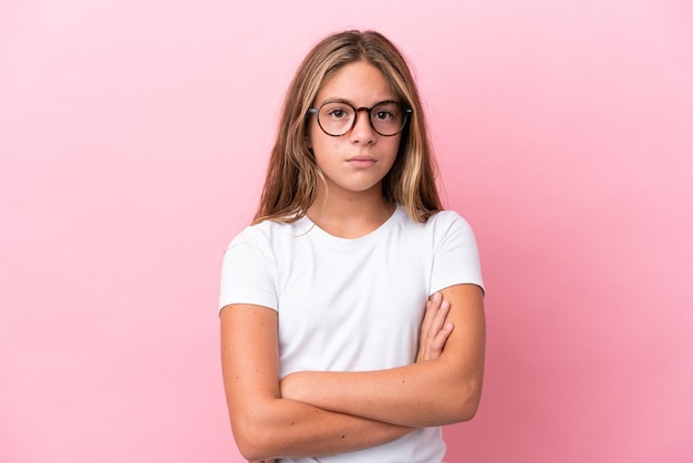 Piccola ragazza caucasica isolata su sfondo rosa con gli occhiali e le braccia incrociate