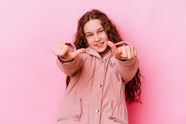 Piccola ragazza caucasica isolata sul colore rosa che alza entrambi i pollici in su, sorridente e sicuro.