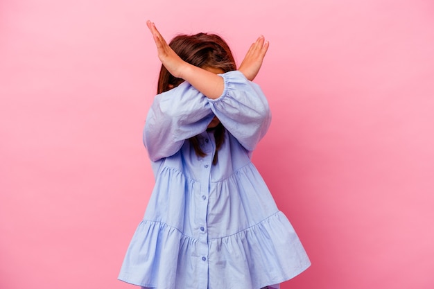 Piccola ragazza caucasica isolata sul colore rosa mantenendo due braccia incrociate, concetto di rifiuto.