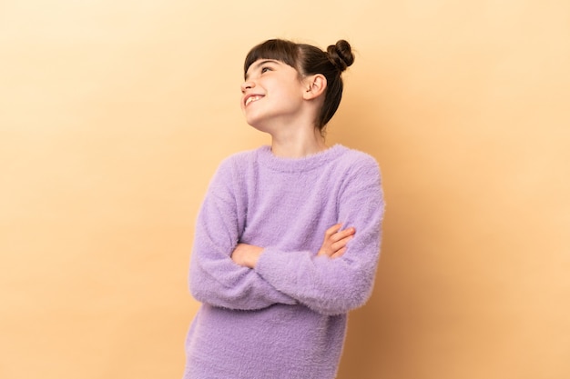 Piccola ragazza caucasica isolata sulla parete beige felice e sorridente