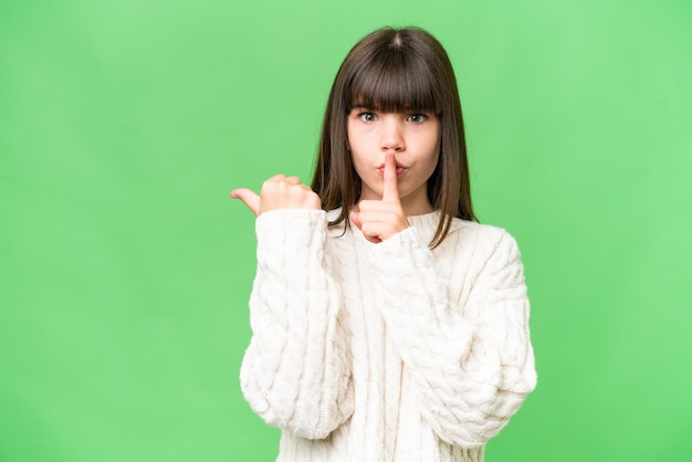 Piccola ragazza caucasica su sfondo isolato che punta al lato e fa il gesto del silenzio