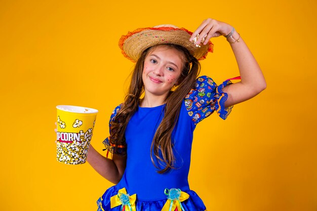 Piccola ragazza caucasica sveglia nel tipico vestito da festa junina che mangia popcorn