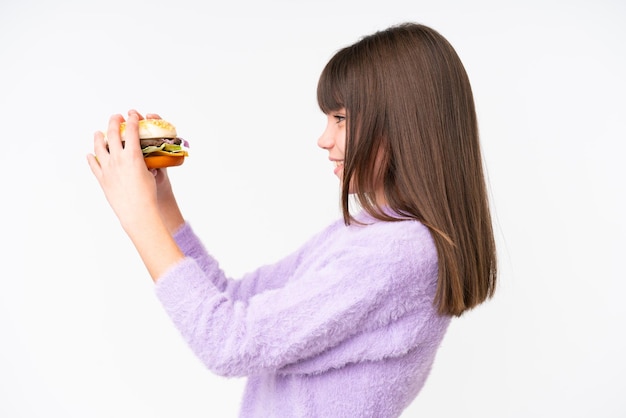 Piccola ragazza caucasica tenendo un hamburger su sfondo isolato con felice espressione
