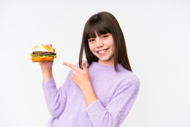 Piccola ragazza caucasica tenendo un hamburger su sfondo isolato e indicandolo