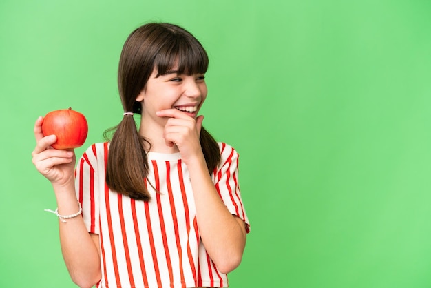 Piccola ragazza caucasica tenendo una mela su sfondo isolato pensando un'idea e guardando il lato